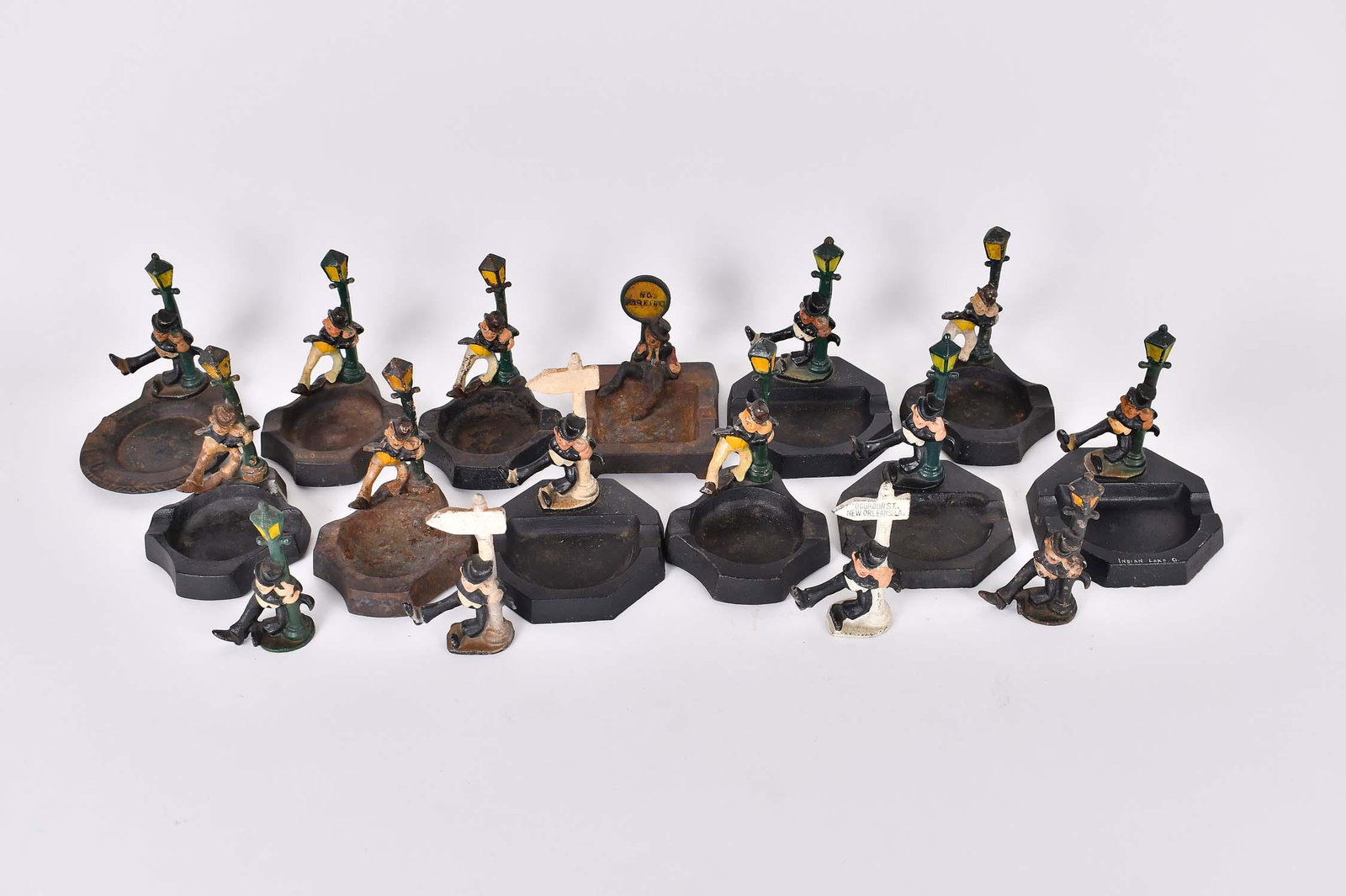 FOURTEEN VINTAGE IRON FIGURAL BAR COLLECTIBLE ASHTRAYS: Circa 1950s. Most depicting a male figure leaning upon either a parking sign, a lamp post or directional, some figures without the ash receiver, variations amongst the group. Heights 3.25 to 4.25 in. 