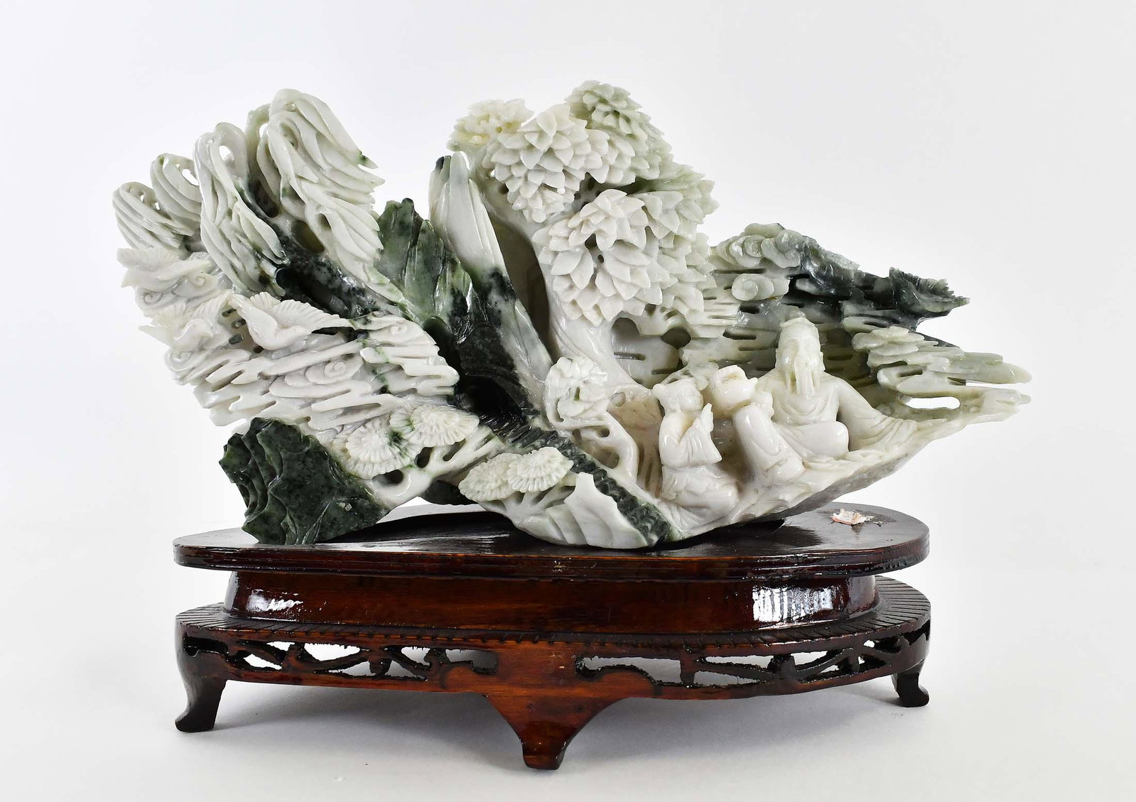 CHINESE SPINACH JADE CELESTRIAL GARDEN GROUP: 20th Century. The green and white striated group with foliage and rockwork set amongst the clouds, and with two deities, on a wood stand. Height of jade 5 in. (approx.) Width 9 in. (approx.) (Cond: on