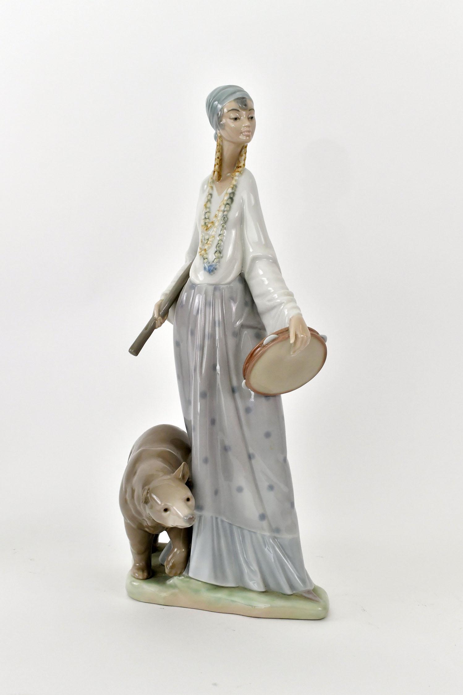 LLADRO PORCELAIN GROUP OF A GYPSY WOMAN: Signed, numbered on the underside. Carrying a tambourine and a staff, a bear at her side. Height 14 in. Width 8 in. (Cond: good)