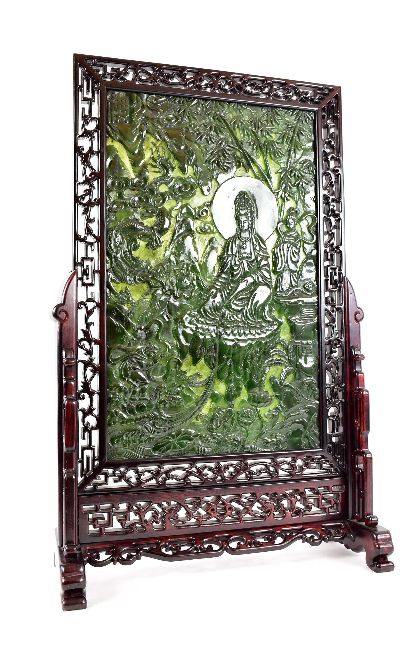 CHINESE SPINACH JADE INSET HARDWOOD TABLE SCREEN: The transparent jade panel depicting Quanyin seated on a rock amidst bamboo in a mountainous landscape, set in a fret carved hardwood stand with trestle supports, Chinese characters sporadically place
