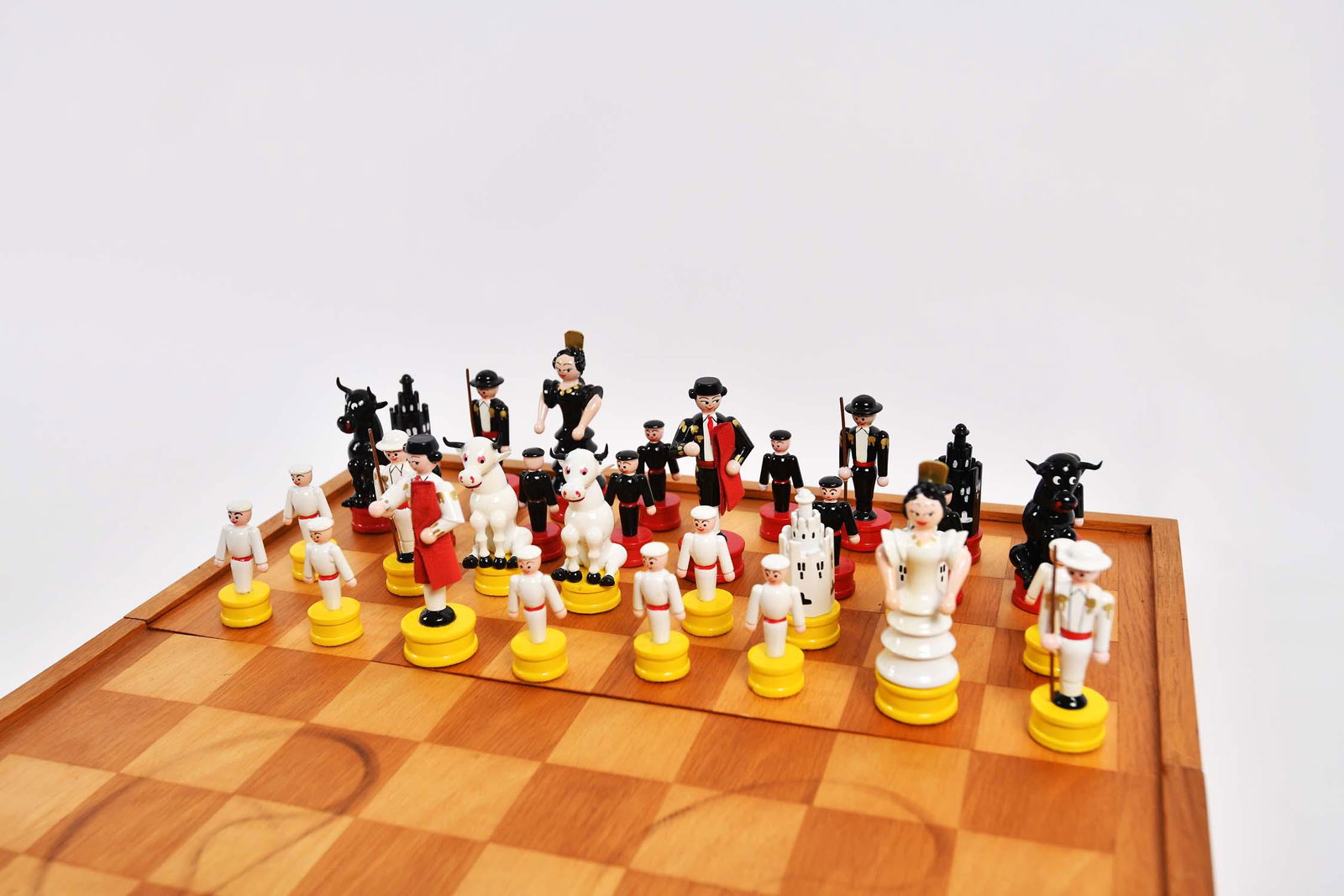CARVED & PAINTED WOOD BULLFIGHT CHESS SET: Circa 3rd Quarter 20th Century. West German made. Painted black or white with red and gilt highlights, with an inlaid hinged chess board, serving as a storage box. Box folded 16 by 8 in. Height of lar