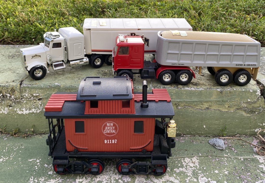 TWO JIM BEAM TRACTOR TRAILERS & A CABOOSE W/ CONTENTS: Vintage, Circa 1975. Each with labels. The trucks and the caboose with their original contents, the trailers and caboose with roofs that slide or lift to reveal the sealed contents, the trailers unhit
