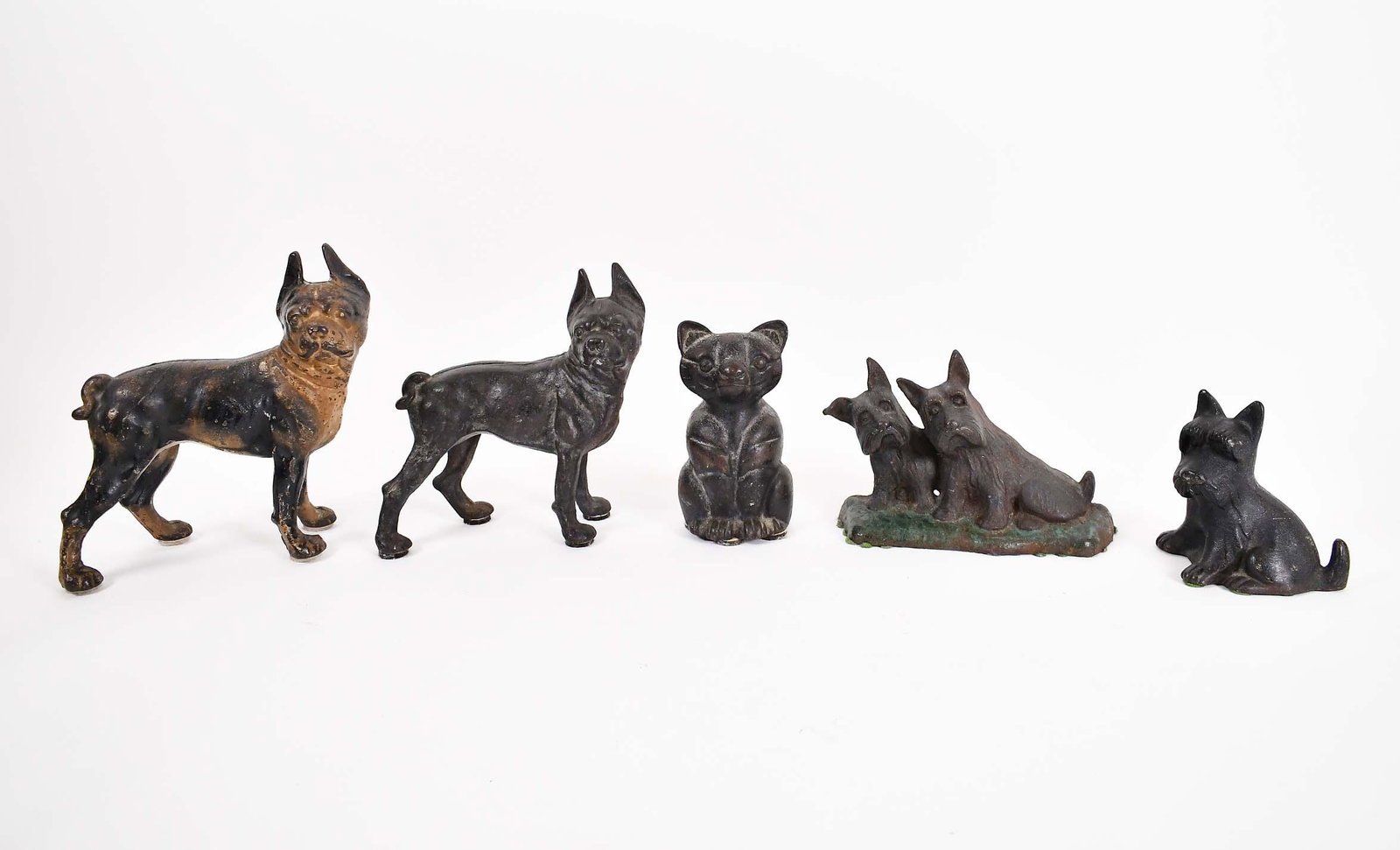 FOUR CAST IRON DOG AND A CAT DOORSTOPS: American/English, 1900 to 1930. Four depicting a terrier or boxer, all painted black, the fifth a cat.Height of largest dog 9.75 in. Width 9.5 in. (Cond: good overall, minor paint loss w/refreshing)