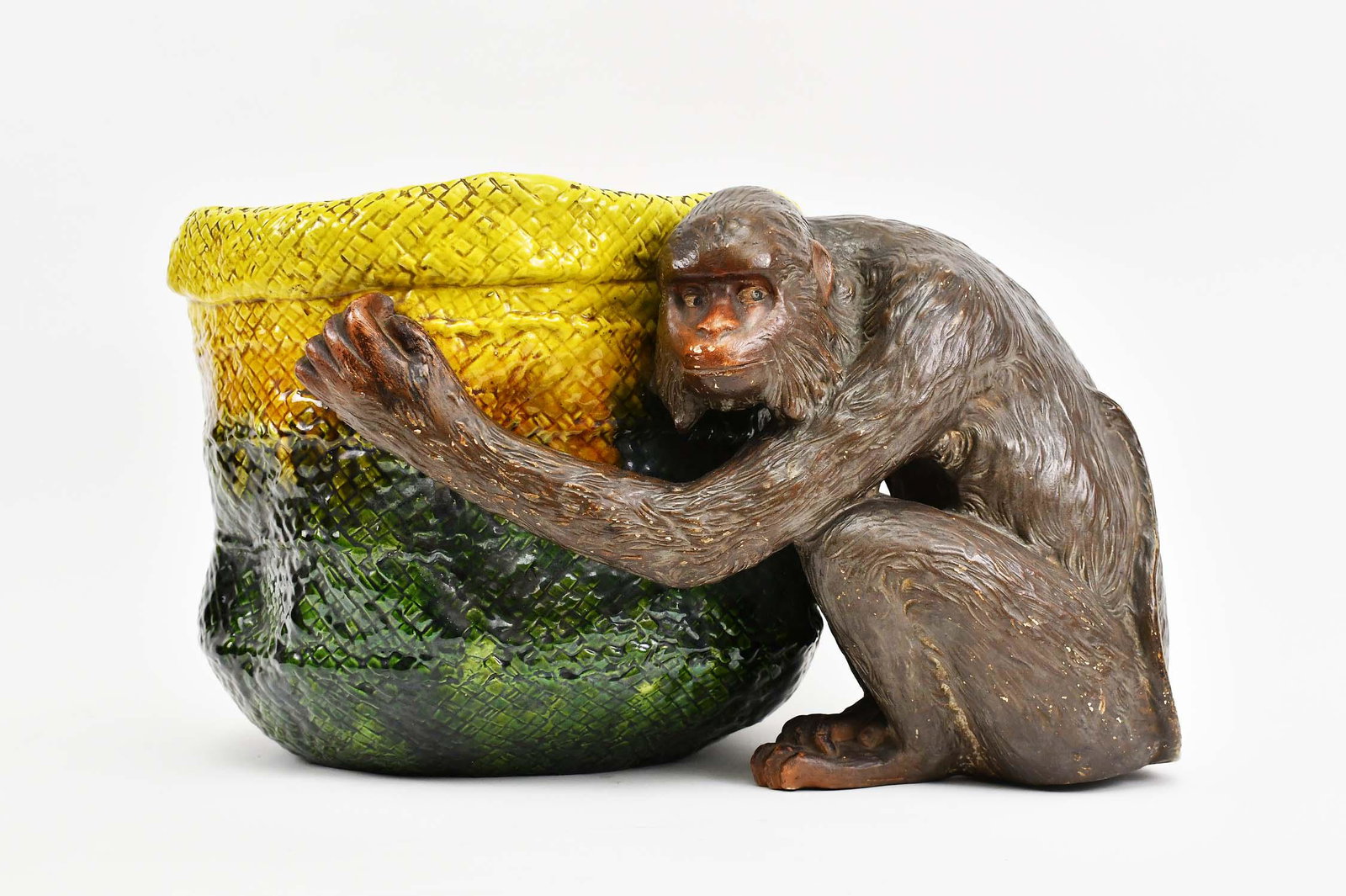ENGLISH MAJOLICA JARDINIERE: Circa 1900. The underside with factory mark, numbered 1251, England, 46937. Modeled as a monkey whose arms wrap around a basket, glazed in brown, yellow and green. Height 12 in. Width 19 in. (Cond: go