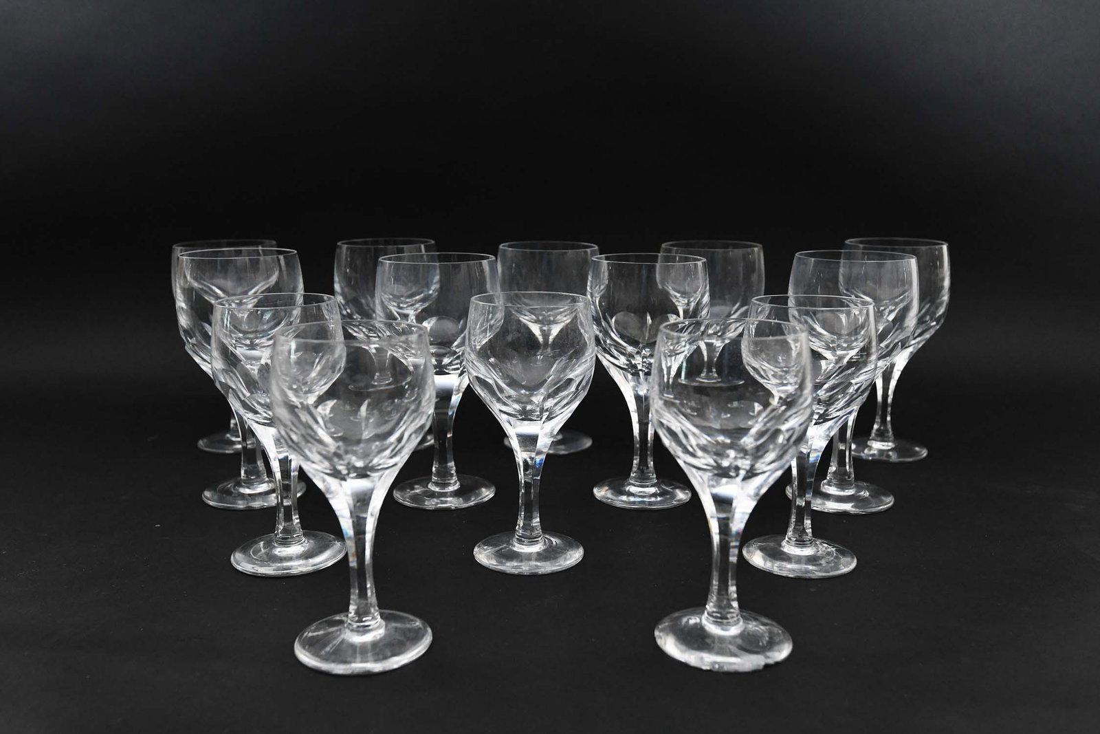 SET OF FOURTEEN COLORLESS WINE GLASSES: In the manner of the Baccarat Harcourt pattern, cut with thumbprints. Comprising: nine red wines and five white wines. Heights 7 in., 6.25 in., respectively. (Cond: good)