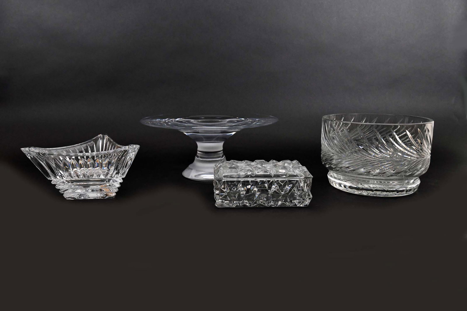 FOUR COLORLESS GLASS TABLE ITEMS: Comprising: a Nambe cake stand, a cut glass circular bowl, a Mikasa triangular bowl and a rectangular molded covered box. Height of cake stand 5 in. Diameter 12 in. Diameter of bowl 8.25 in. (Cond: al