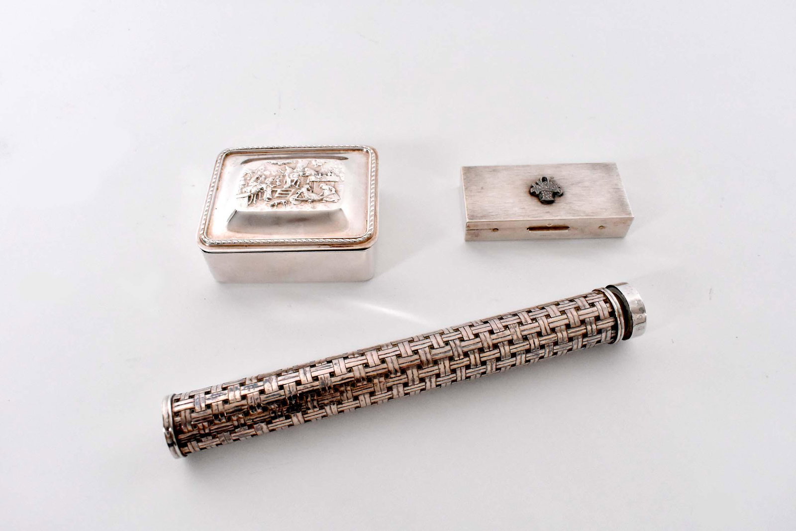 THREE STERLING SILVER OBJECTS: Early to Mid-20th Century. Comprising: a basket-woven cylindrical cigar case, with Continental markings, a rectangular box, marked Sterling, applied with a silver flower-filled basket, and another rec