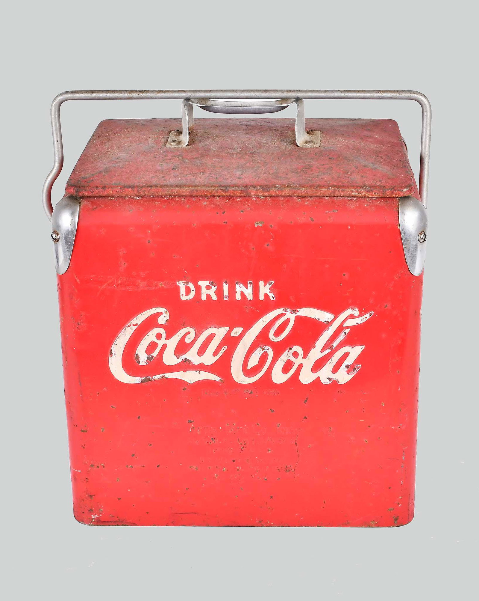 VINTAGE COCA-COLA PAINTED METAL PICNIC COOLER: Circa 1940-1950. The red painted rectangular case with white lettering, with a stabilizing bail and lift handle, the lid opening to a zinc-lined interior, the exterior corners with aluminum mounts, on