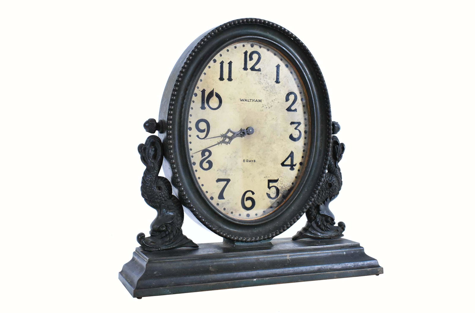 WALTHAM PATINATED METAL EIGHT-DAY MANTLE CLOCK: Early 20th Century. The dial marked. In a neoclassical style, oval, with dolphin supports. Height 12.25 in. Width 12 in.