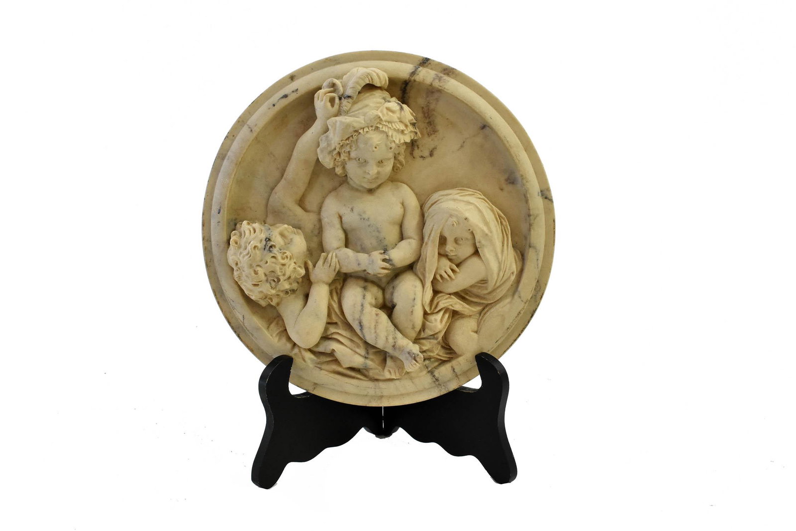 ITALIAN RENAISSANCE STYLE CARVED MARBLE ROUNDEL: Late 19th Century. The circular black veined marble relief carved with three playful putti, one with a feathered headdress sitting atop another, the third wrapped rapped in a blanket, the reverse set 