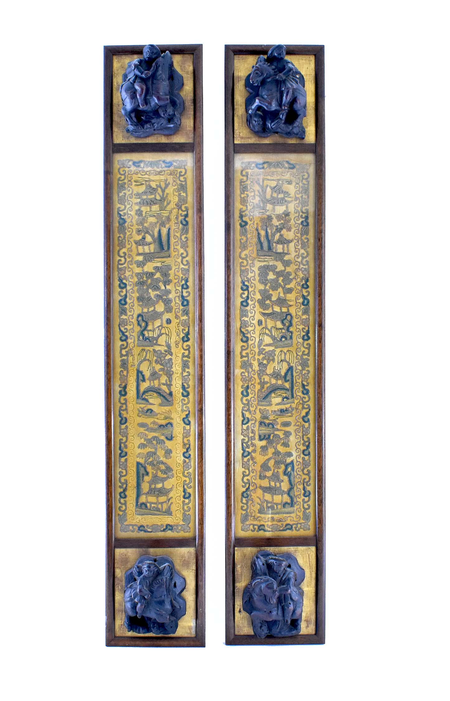 PAIR OF CHINESE GILT AND SILK EMBROIDERED SLEEVE PANELS: Qing Dynasty. The panels woven with landscapes within scrolled borders, on a vertical plane, within a glazed plate, the upper and lower ends affixed with walnut corbels carved with a rider on horsebac