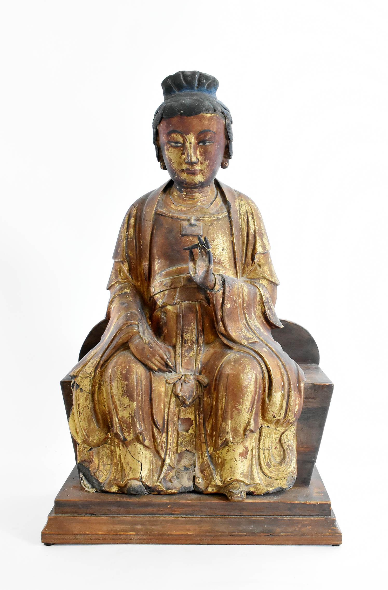 CHINESE GILT LACQUER SEATED BUDDHA: 17th/19th Century. Draped in elaborate gowns, his hair tied up, seated with legs spread, one hand on the right knee, the other raised in a teaching gesture, seated upon a wood base. Height 22 in. Widt