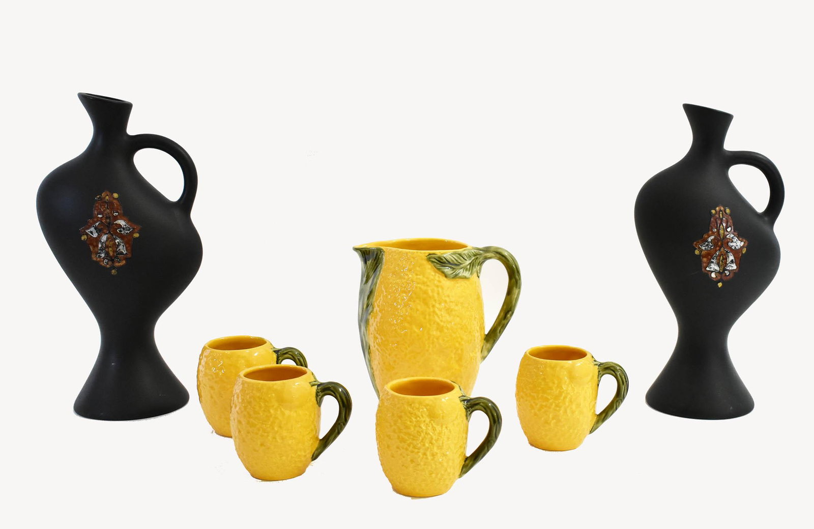ITALIAN EARTHENWARE LEMONADE SET AND TWO VASES: The lemonade set represented as lemons, comprising four cups and a pitcher; the vases, of undulating form, with a loop handle, with an applied stylized motif on a black mat ground. Height of lemonade 