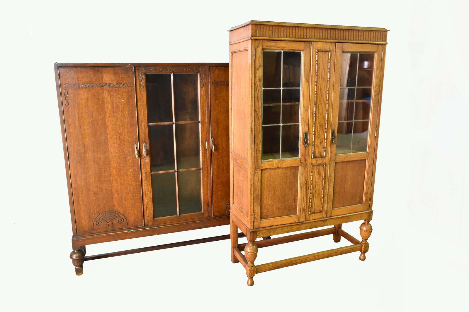 TWO JACOBEAN STYLE OAK SIDE CABINETS: Early 20th Century. One with two parcel glazed doors with beaded borders; the second with a center glazed panel flanked by doors, both on turned supports, joined by stretchers. The first, Height 61.5 