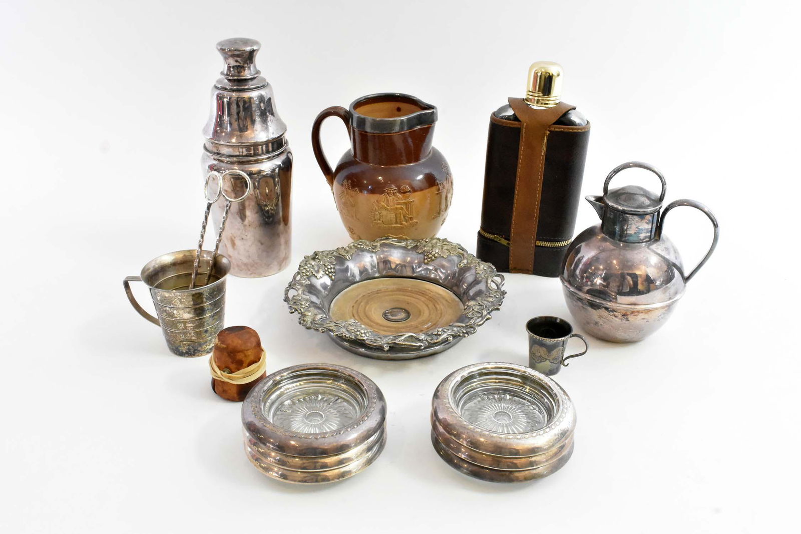 GROUP OF GENTLEMEN BAR AND TABLE ACCESSORIES: Comprising: a Leather-Covered Flask, an English Silver-Mounted Salt Glazed Stoneware Pitcher, a Jigger, Two Small Leather-Bound Cups, a Silver Plate Spherical Lidded Jug, a Bottle Coaster, Two Silver