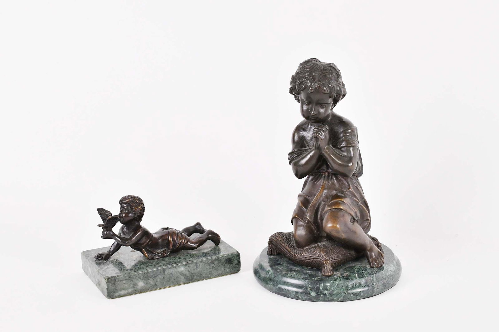 TWO CONTINENTAL PATINATED FIGURAL BRONZES: Late 19th/Early 20th Century. The first, a young girl kneeling upon a cushion, with downward cast eyes, hands clasped, on a circular marble base. The second, of a scantily clad boy in repose, kissing 
