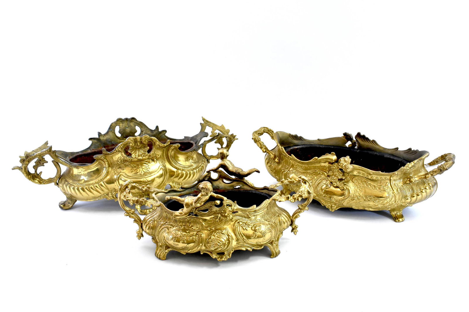 THREE FRENCH ROCOCO STYLE GILT BRONZE JARDINIERS: First Half 20th Century. Each of similar shape cast with foliage, reserved with figures, armorial devices, shells and scrolls, one surmounted by two putti, all three with double handles, on scrolled f