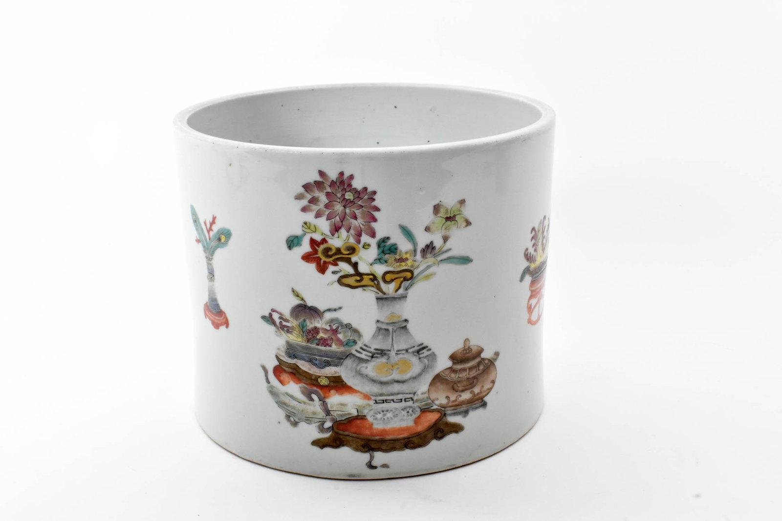 CHINESE ENAMEL DECORATED PORCELAIN BRUSH POT: Qing Dynasty, 18th Century. The underside unmarked but with a label, Connoisseurs Store, Melbourne, 279-36. The cylindrical pot decorated with a foliate-filled vase and various depictions of antiques.