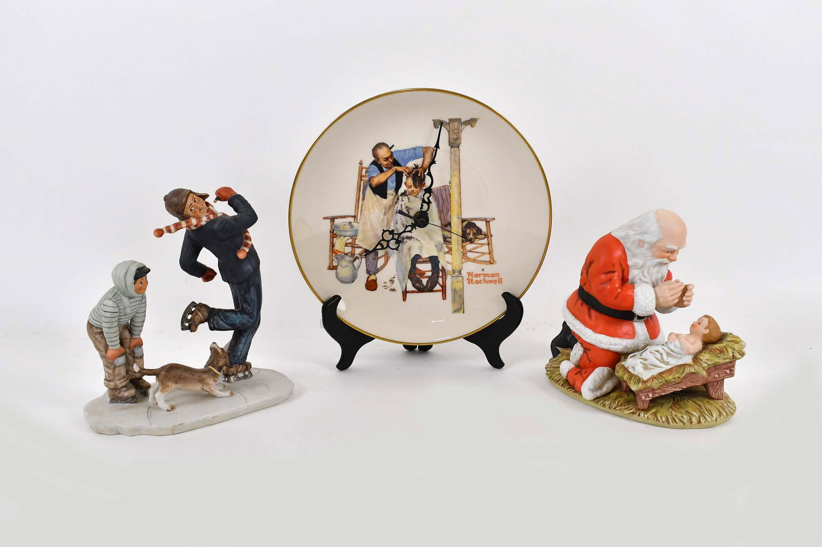 THREE NORMAN ROCKWELL PORCELAIN COLLECTIBLES: Each marked. Comprising: a figure of Santa Claus praying before the Christ Child in a crib, two boys ice skating with their dog and a clock containing a barber shop scene. Height of figures 7.5 in., 8