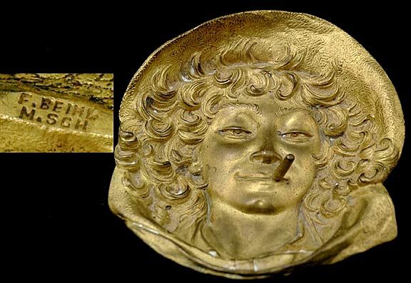 German Antique Bronze Relief Tray Lady Smoking Cig: German Antique Bronze Relief Tray. Cast Gilt Bronze Tray Depicting Head of a Huck Finn type Character Woman Smoking a Cigar, Flowing Curly Hair with Hat Down to Collar with Ties. Signed Lower Right: G