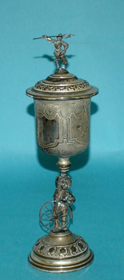 VICTORIAN SILVER PLATED CUP AND COVER: VICTORIAN SILVER PLATED CUP AND COVER 19th Century. The scroll engraved bowl supported by a young boy holding a large wheel, the cover with a soldier holding a lance and a stein. Height 13 1/2". (200/