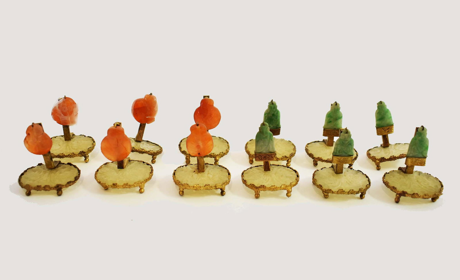 SET OF TWELVE JADE AND CORNELIAN PLACE CARD HOLDERS: With gilt metal mounts. Each oval stone variously carved. Height 1 in. (Cond: one stone detached)
