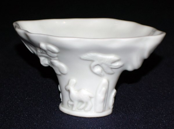 VERY FINE BLANC DE CHINE PORCELAIN LIBATION CUP: VERY FINE BLANC DE CHINE PORCELAIN LIBATION CUP Chinese. Qing Dynasty. 17th/18th Century. Molded with a dragon, birds and animals and a tree. Height 3". Length 5 1/2". Provenance: T.Y. King & Sons, Lt