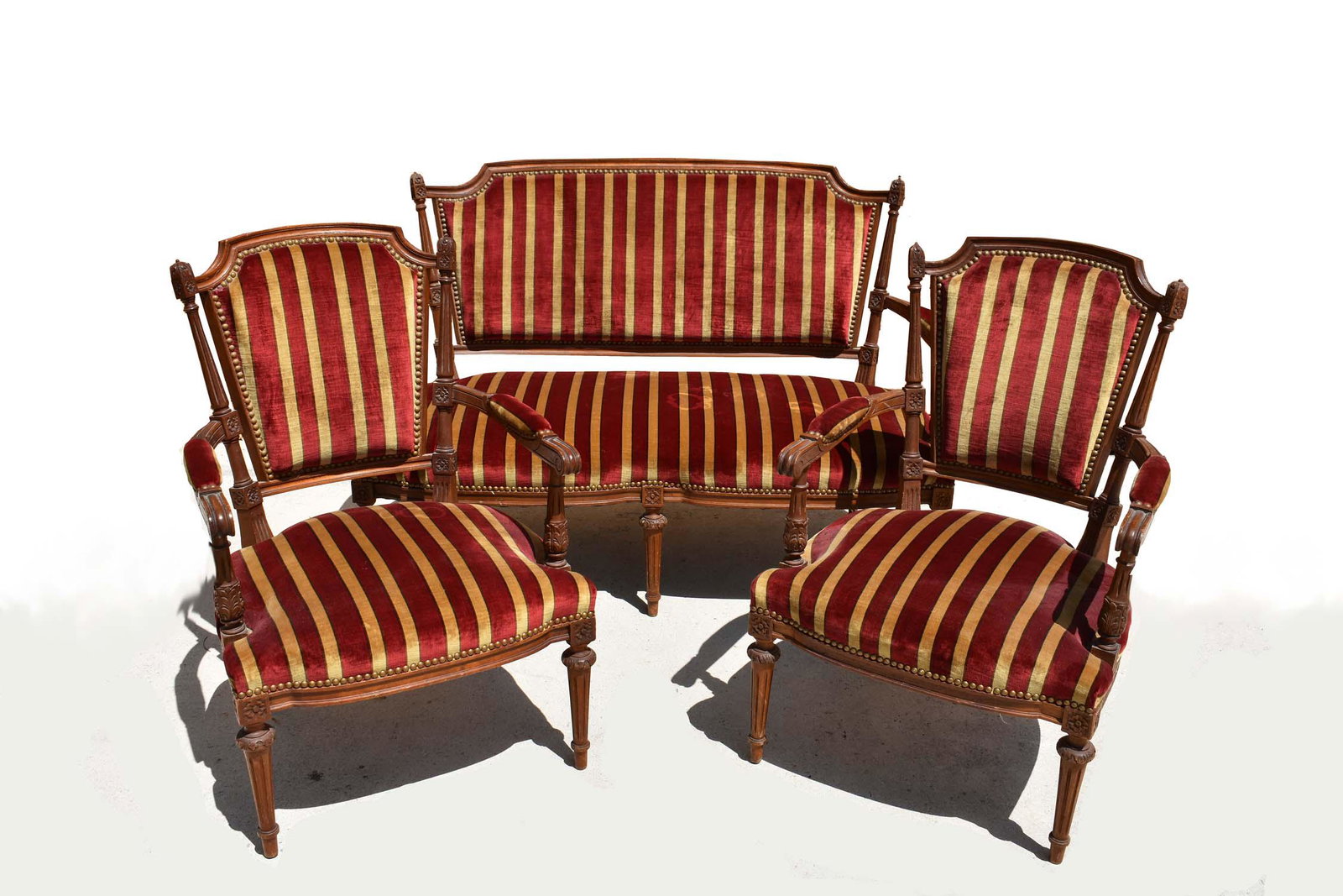 SUITE OF LOUIS XVI STYLE BEECHWOOD SEAT FURNITURE: Early 20th Century. Comprising a pair of fauteuils and a settee; each with leaf tip borders, with upholstered square back and seat, on circular tapering fluted legs, upholstered in a burgundy stripe. 