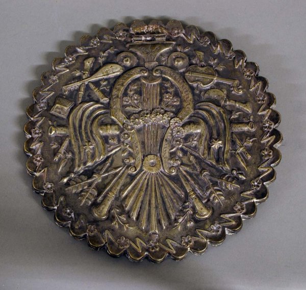 GOOD MIDDLE EASTERN TABLE MIRROR: Syrian. The circular mirror plate set in a scalloped frame with a solid silver plated back (post missing). Embossed in the French manner with cannons, musical instruments, arrows and flowers. Diameter