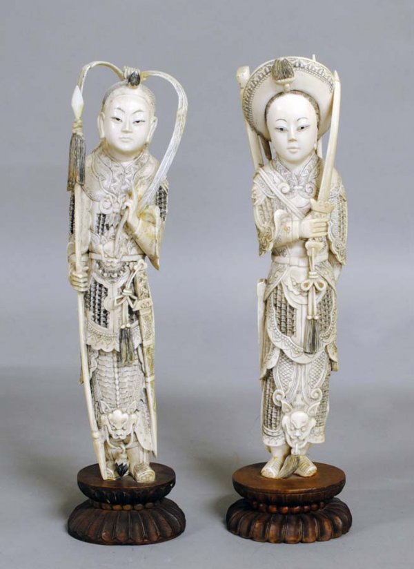 PAIR OF CARVED IVORY FIGURES OF WARRIORS: Chinese. Each male and female dressed in armor, one holding a lance, the other a sword, raised on double lotus wood bases. Height 11 7/8". (Cond: each with minor imperfections) (500/700)