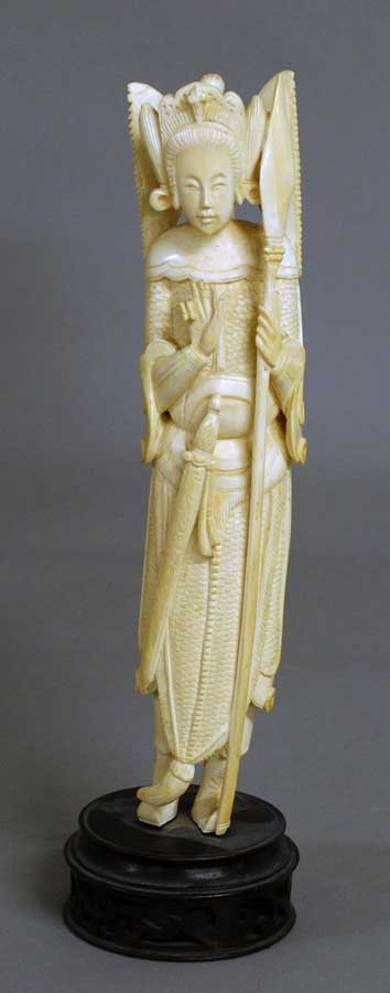 CARVED IVORY FIGURE OF A LADY WARRIOR: Chinese. 20th Century. In a standing position wearing full armor and holding a lance. Height 10". On a carved wood stand. (300/400)