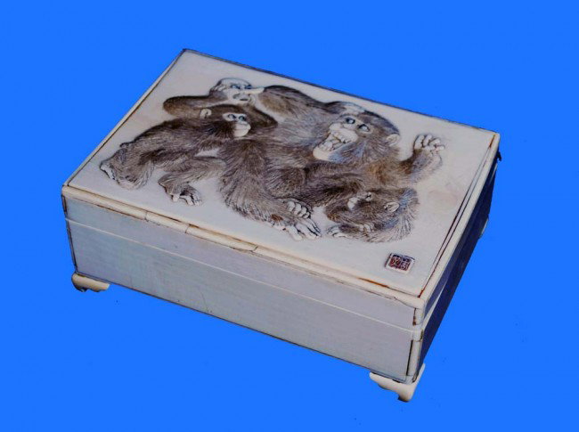 WELL CARVED IVORY BOX AND COVER: Japanese. Meiji-Period. 19th Century. Signed in a seal. Of rectangular shape, the cover finely carved with a group of three monkeys, one holding a human mask. Length 6 ¾". (1000/1500) (NOTE: INTERNAT