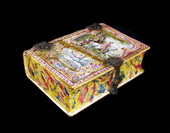 LILLE SOFT-PASTE BOOK FORM BOX: French. 18th Century. With metal mounts, painted with a figural and a rural scene. Length 8 1/4". (Cond: restored) (300/400)