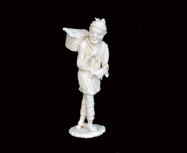 CARVED IVORY FIGURE OF A FISHERMAN: Japanese. Meiji-Period. 19th Century. Signed. Wearing a short jacket and straw skirt, carrying a woven basket and a fish. Height 9 ¼". (1200/1600) (NOTE: INTERNATIONAL SHIPPING IS NOT AVAILABLE FOR T