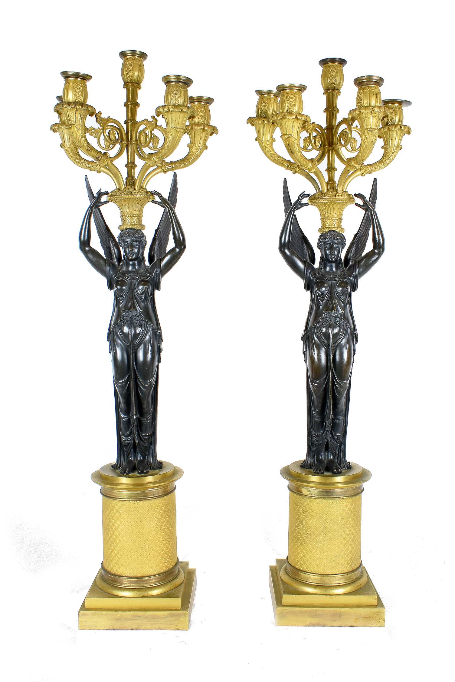 PAIR OF CHARLES X PATINATED BRONZE CANDELABRA: French. Manner of Thomire. Mid to late 19th Century. Each with a classically-clad female figure, arms raised holding aloft a fruit-filled basket supporting a five-light candelabra, atop a circular col
