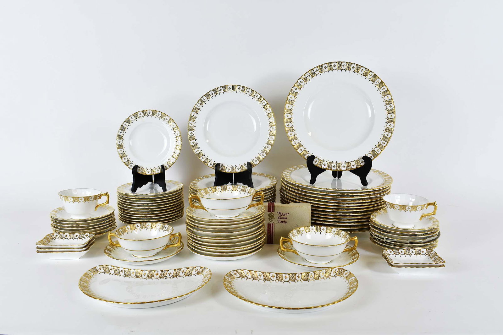 ROYAL CROWN DERBY 105 PIECE PORCELAIN DINNER SERVICE: First-half 20th Century. Factory marks on the underside. Each element with a cream glazed body, the rim with gilt highlights. Comprising: fourteen dinner plates, fourteen luncheon plates, fourteen bre