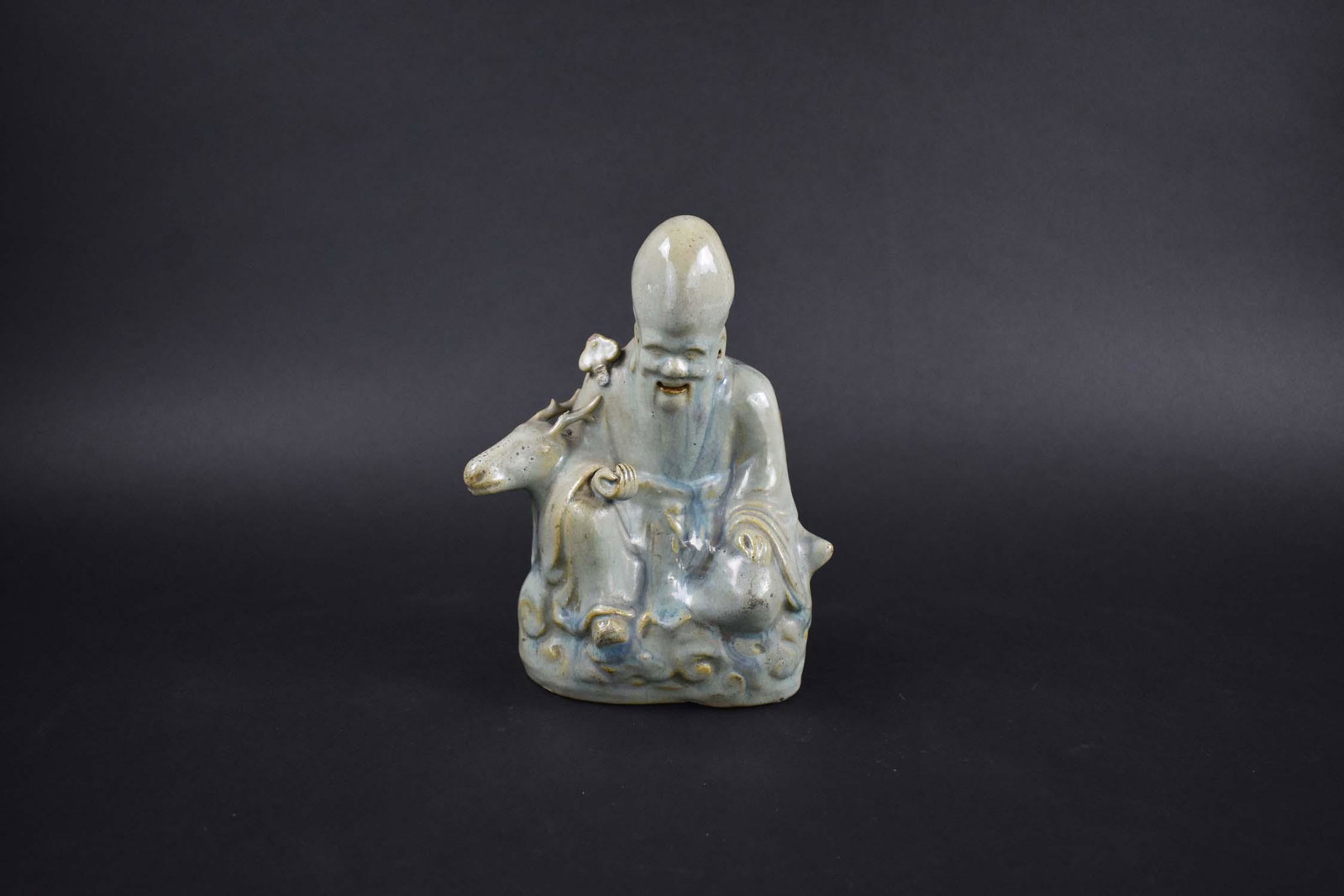 CHINESE QING DYNASTY POTTERY FIGURE OF SHOU LAO: Chen Lung Period. Partial label, Maison Satuma. The deity seated upon clouds a deer by his side, as he holds a ruyi scepter, with a bluish celadon crackle glaze. Height 8 in. Width 6.75 in. Depth 2.75