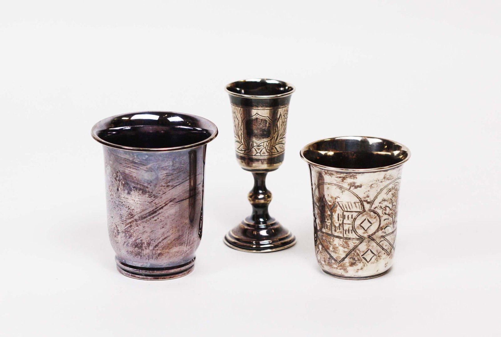 CONTINENTAL SILVER KIDDUSH CUPS & TWO DANISH: Silver Beakers The first, a kiddush cup with an etched blank cartouche flanked by foliage, on a circular spreading foot, marked. The second a Russian 84 marked beaker, incised with two village scenes.