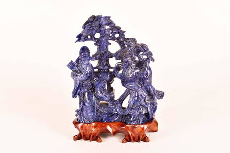 CHINESE LAPIS LAZULI FIGURAL GROUP: Depicting a man and woman, with wind-blown draperies, before a pagoda and tree, on a carved wood stand. Height 7 in. Width 6 in.