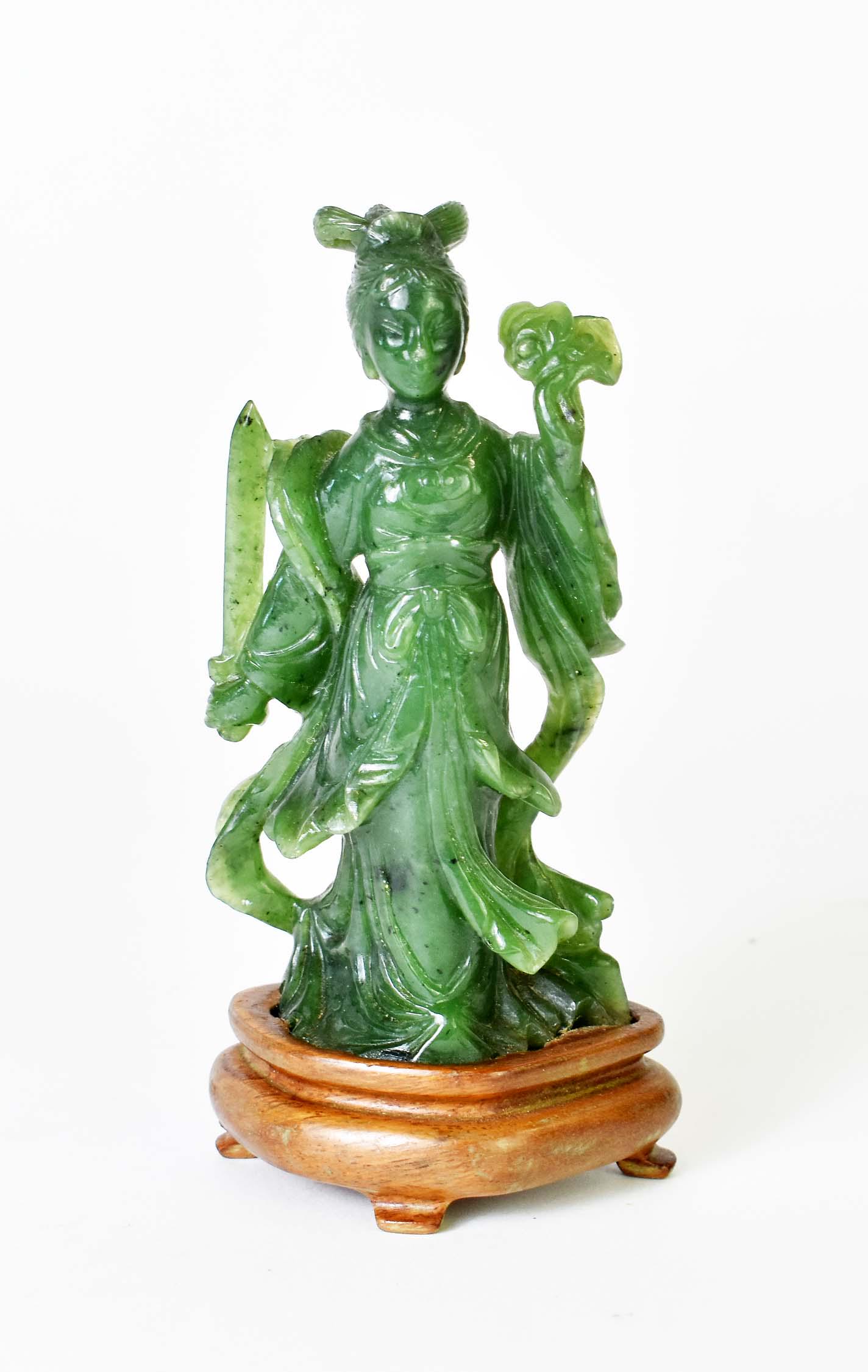 CHINESE SPINACH JADE QUANYIN: Dressed in elaborate robes, holding a sword in one hand and a Ruyi Scepter in the other, on a wood stand. Height 4.75 in., overall 5.5 in.