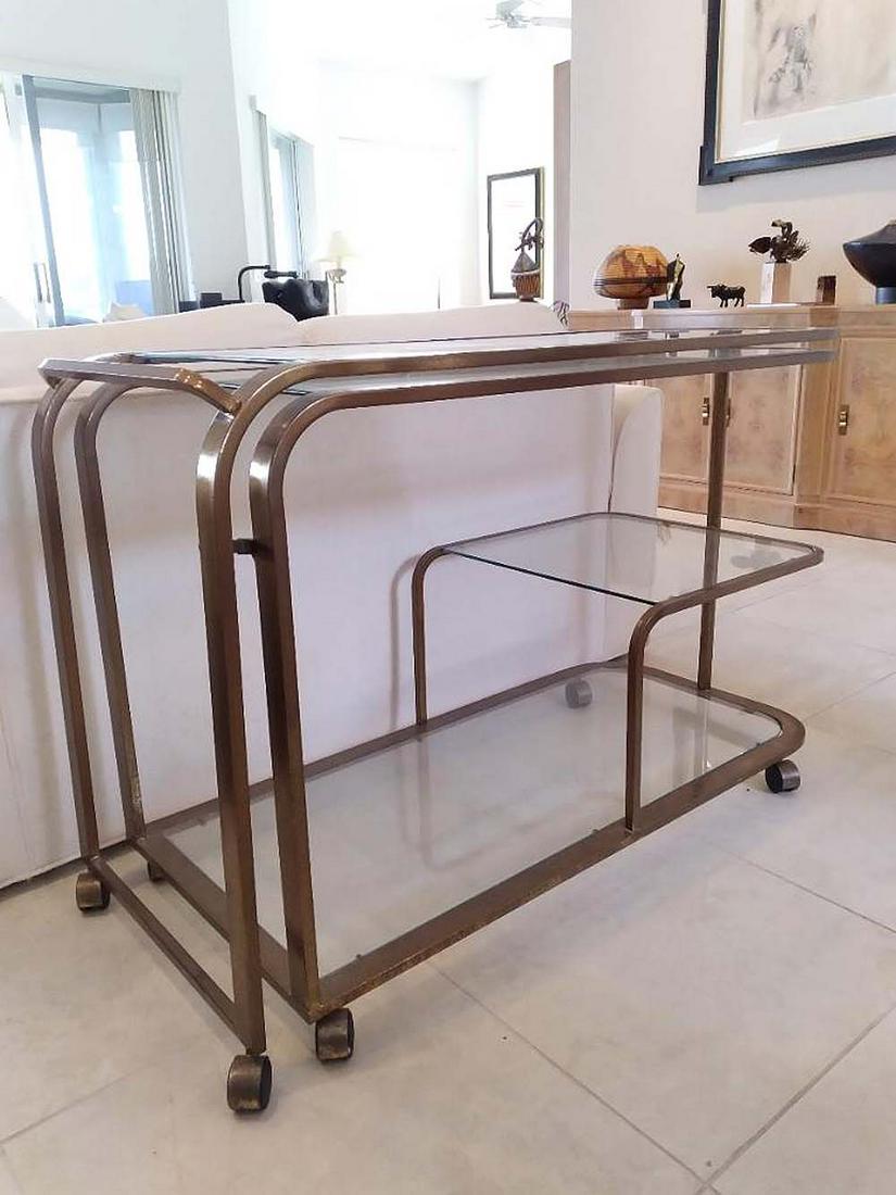 MODERNIST BRASS & GLASS ADJUSTABLE BAR CART: Circa 1970. Rectangular in form, with glass inset tops, hinged at the center opening to increase the horizontal surface. Height 29 in. Width closed 44 in. Width open 86 in. Depth 19 in.