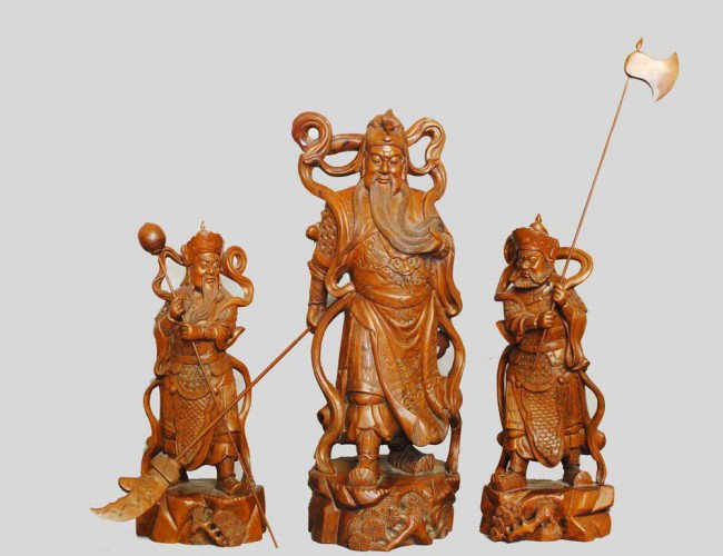 GROUP OF THREE CARVED BOXWOOD FIGURES: Chinese. Each of a warrior immortal holding a weapon, raised on a naturalistic base. Heights 11 1/2" to 15 1/2". (600/900)