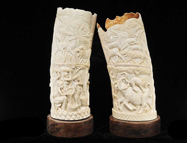 PAIR OF AFRICAN IVORY TUSK VASES: Each carved with various animals and one also with a village scene. Heights 13 1/2" and 14 1/2". On wood stands. (400/600)