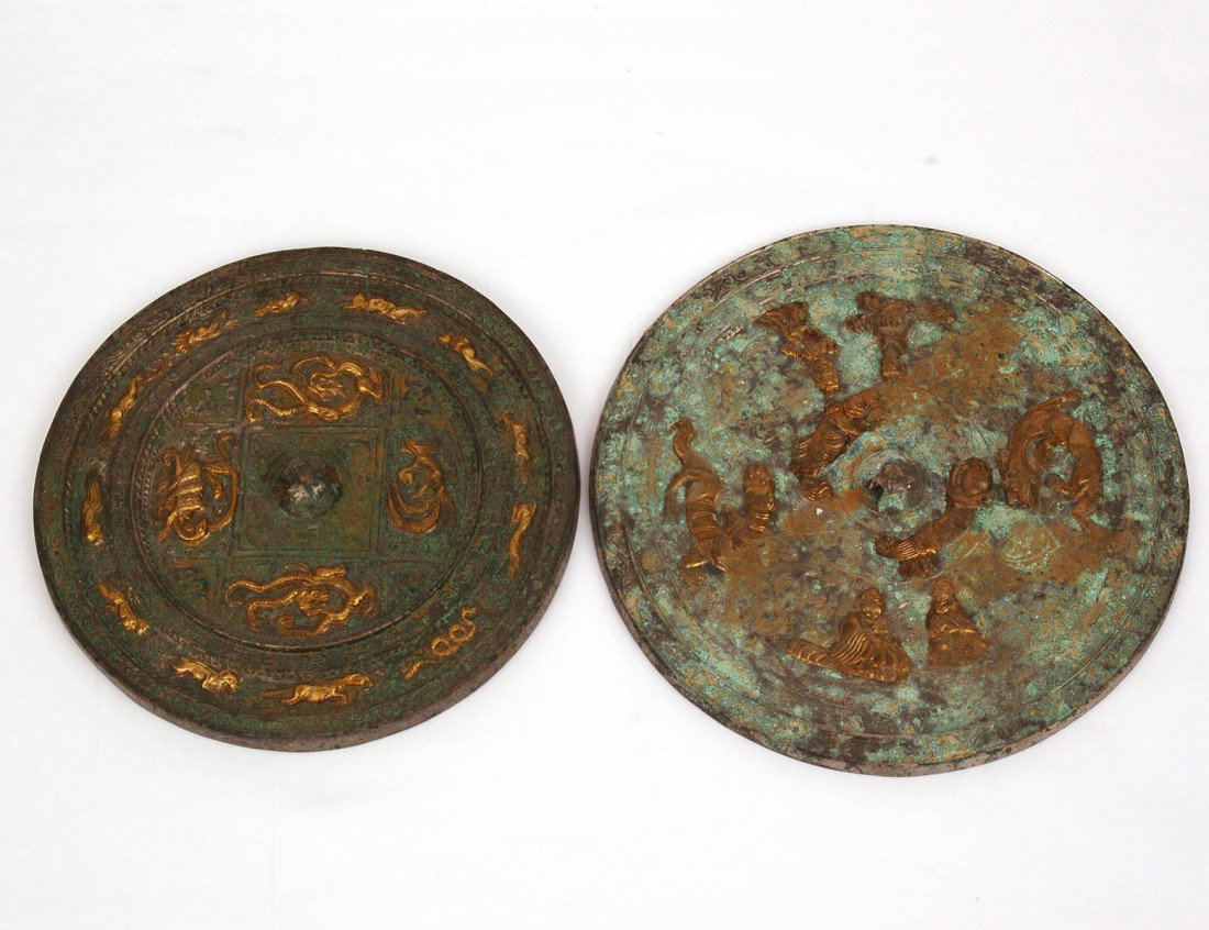 TWO PATINATED AND PARCEL GILT BRONZE HAND MIRRORS: Each of circular shape, one cast with figures and animals, the other cast with the signs of the Zodiac. Diameters 8 18" and 8 7/8" (500/700)