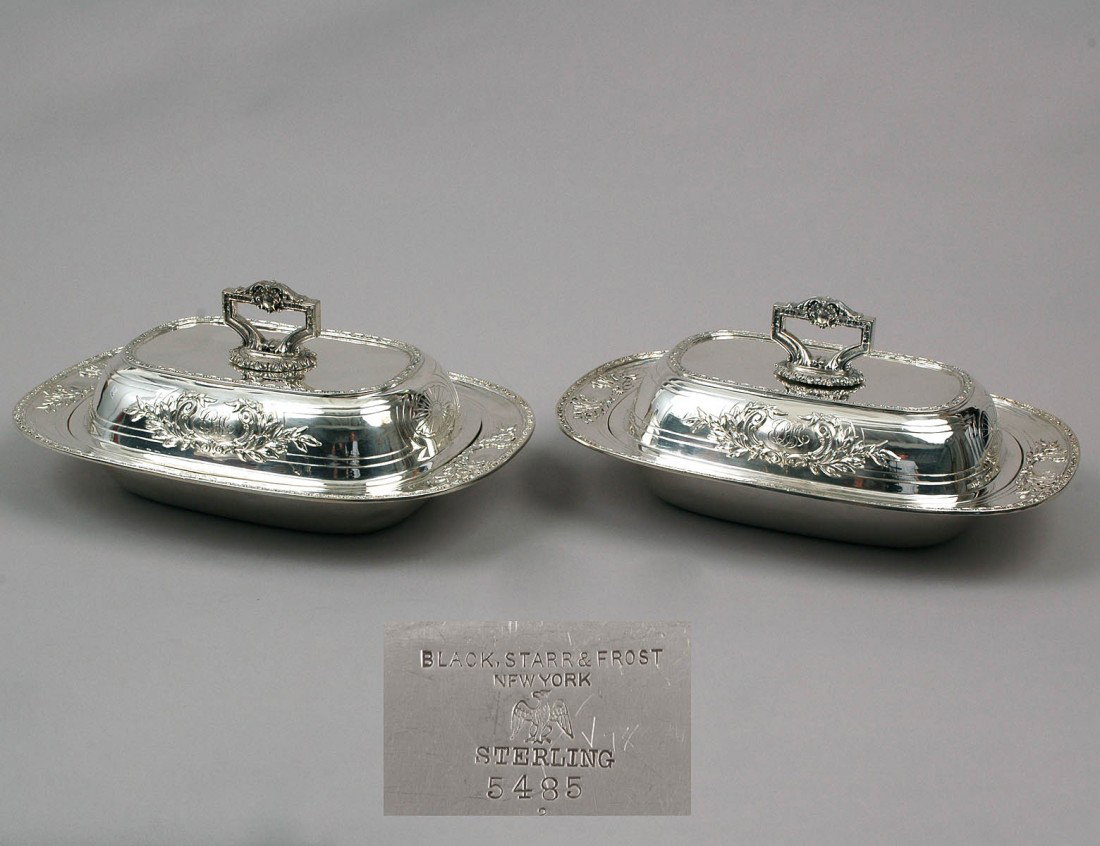 PAIR OF STERLING SILVER ENTREE DISHES AND COVERS: American. 1876-1929. Makers: Black, Starr & Frost. Each dish centered by a conjoined monogram, the cover with detachable handle and floral shield with monogram. Length 11 1/4". (64 oz) (2500/3500)