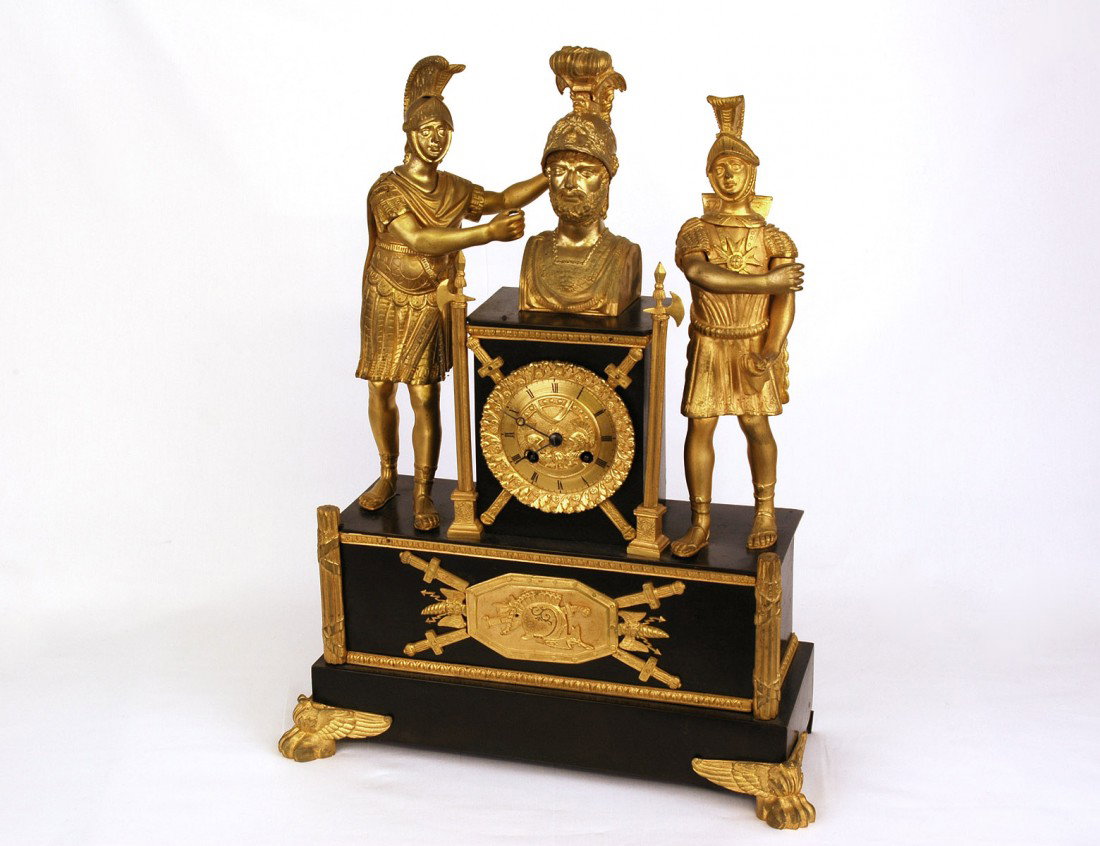 CLASSICAL REVIVAL GILT AND PATINATED BRONZE MANTEL: French. 19th Century. The circular sculptured dial with Roman numerals surmounted by a Roman bust and flanked by soldiers, raised on a rectangular base with winged paw feet. Height 19 5/8". Length 15 