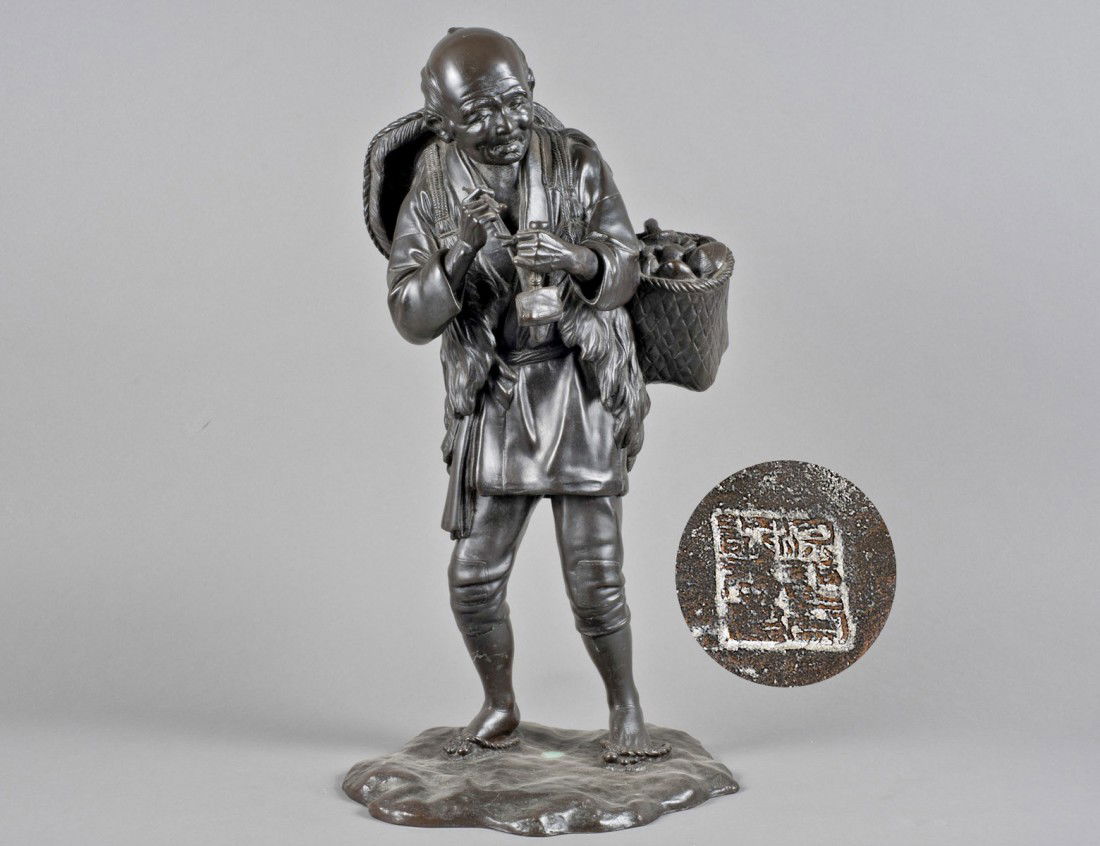 PATINATED BRONZE FIGURE OF A FARMER: Japanese. 20th Century. Signed within a seal. Walking in a field wearing a short jacket, fur and a large hat on his back, carrying a basket of mushrooms and holding a pipe and tobacco pouch. Height 19