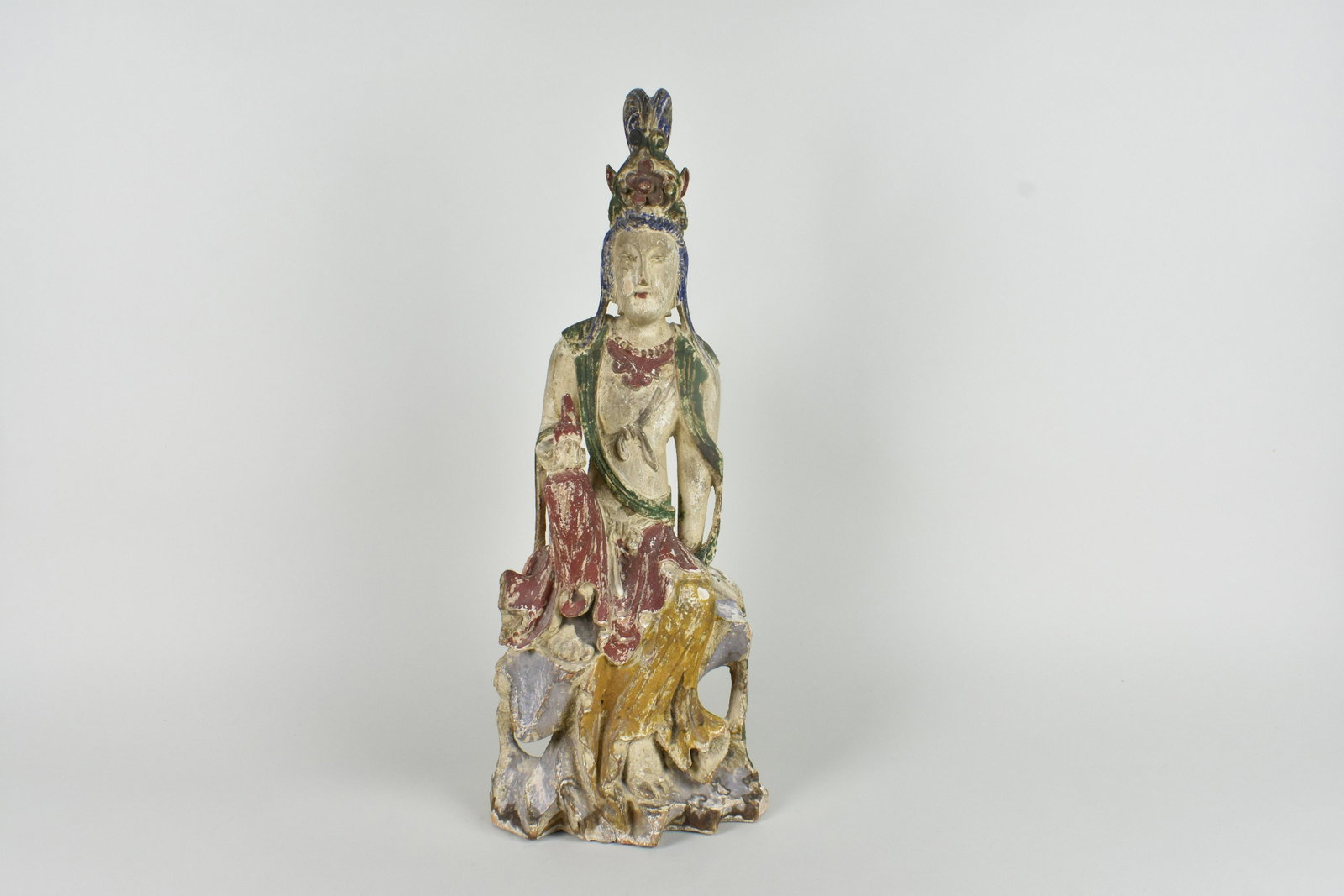 CHINESE POLYCHROMED WOOD FIGURE OF QUANYIN, Elaborately dressed, seated upon rockwork, and holding a: CHINESE POLYCHROMED WOOD FIGURE OF QUANYIN Elaborately dressed, seated upon rockwork, and holding a peach. Height 22.5 in., Width 7.5 in.