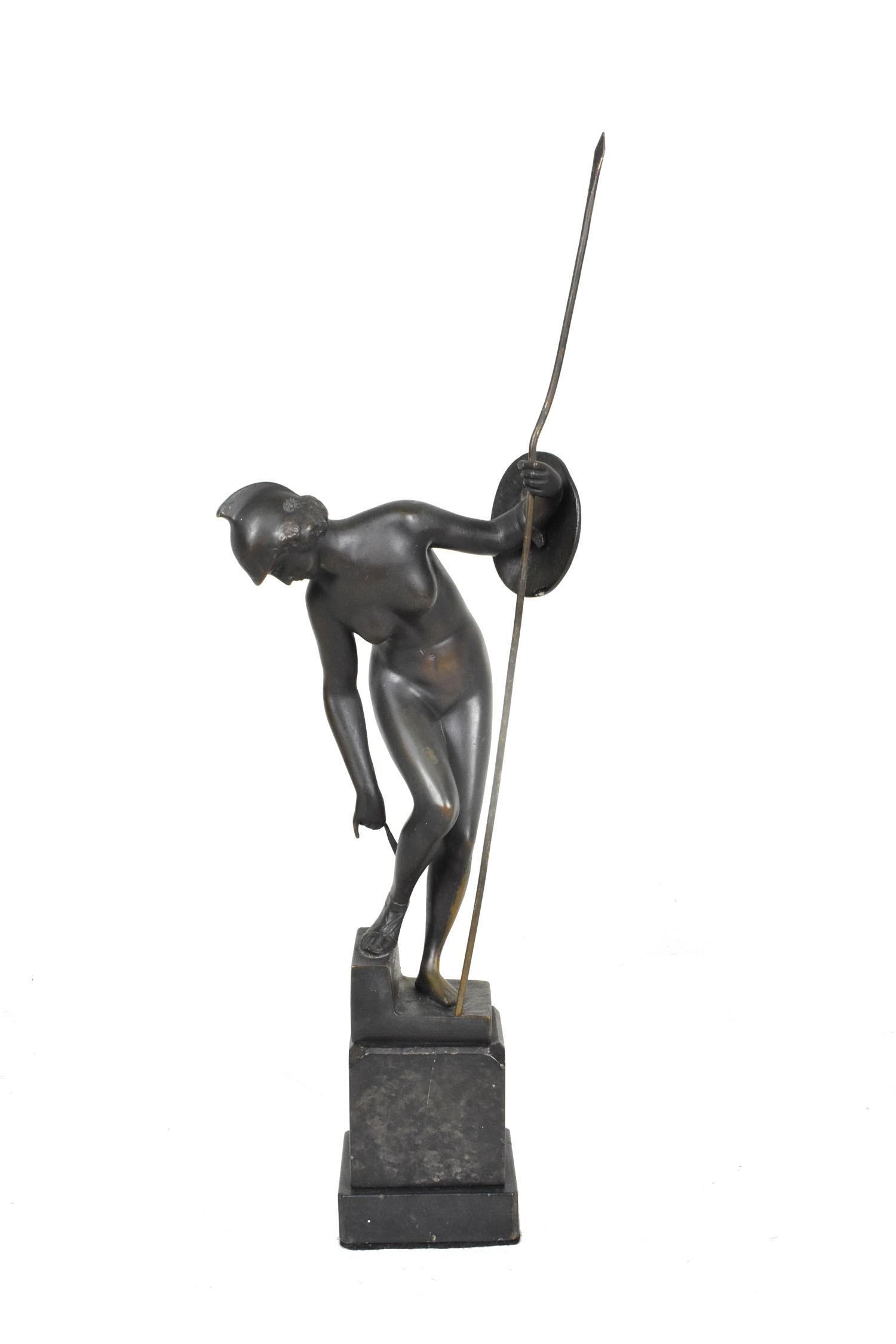 GRAND TOUR PATINATED BRONZE FIGURE OF MINERVA, Early 20th century. The helmeted nude adjusting her: GRAND TOUR PATINATED BRONZE FIGURE OF MINERVAEarly 20th century. The helmeted nude adjusting her sandals, holding a spear and shield, on a stone base. Height overall, 16.5 in., Width 5.5 in.