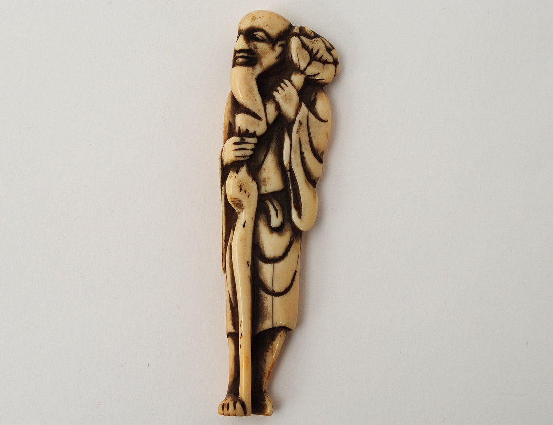 WELL MODELED IVORY NETSUKE OF A SAGE: Japanese. Edo-Period. 18th Century. The elongated Buddhist elder holding a lotus flower and a gnarled staff. Height 3 1/2". (500/800)